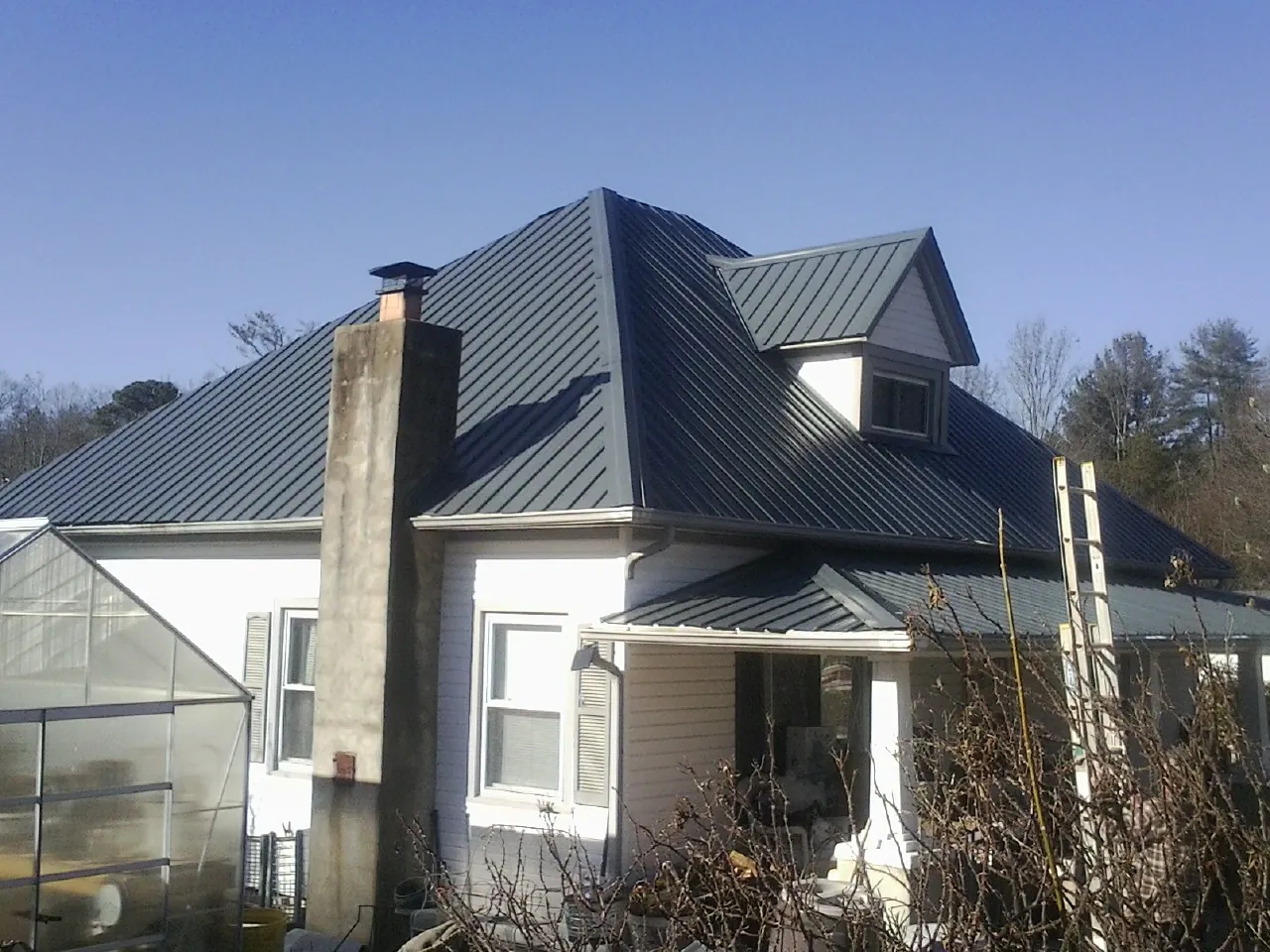Dark blue standing seam metal roof on a white farmhouse with dormer — Slate & Tile Roof Repair by Roofing Brothers in Carlos