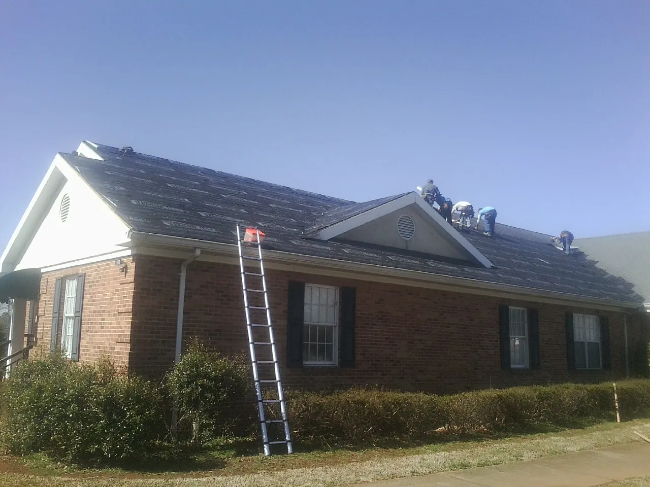 Crew tearing shingles off a brick ranch roof with a ladder set — Emergency Roof Repair work by our crew in Carlos