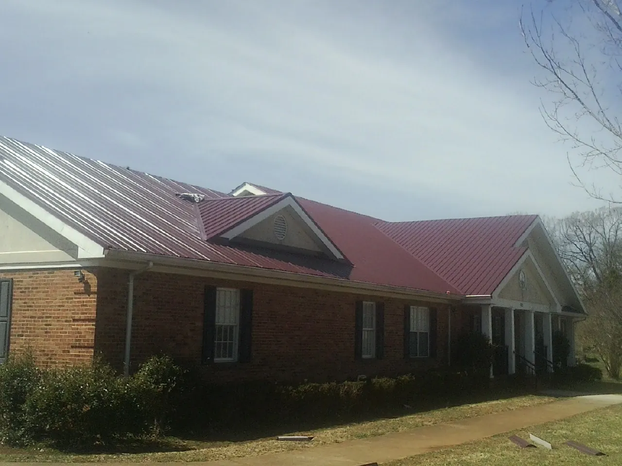 Red metal roof with gabled entries on a long brick building, from a Hail Damage Roof Repair job in Carlos