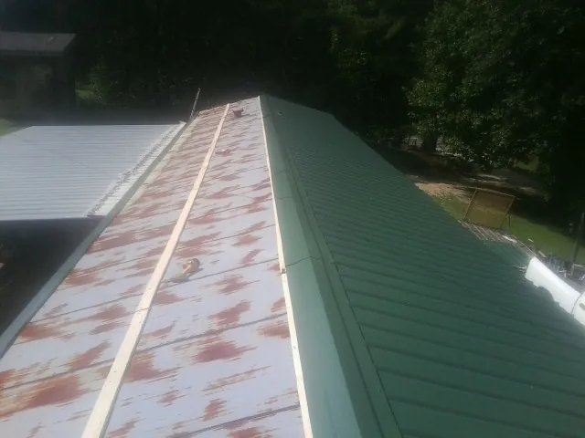 Old rusted panels beside newly installed green metal roofing — Wind Damage Roof Repair by Roofing Brothers in Carlos