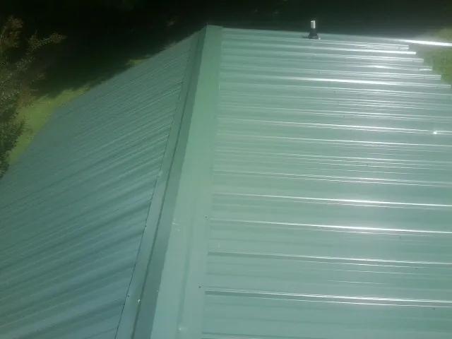 New green metal panels meeting at the ridge of a roof — Flat Roof Repair work by our crew in Carlos