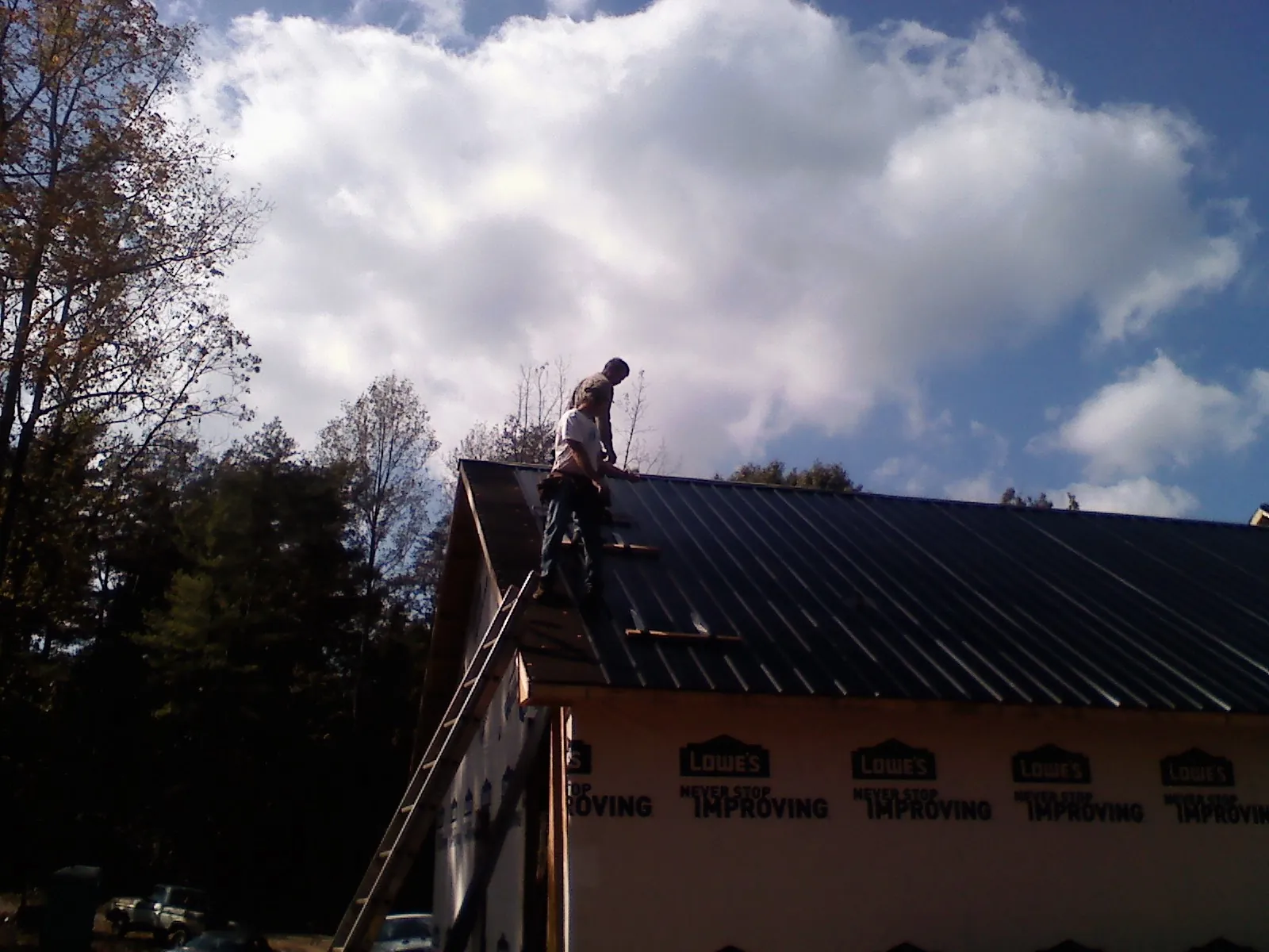 Roofer fastening dark metal panels high against a cloudy sky, from a Roof Inspection job in Carlos