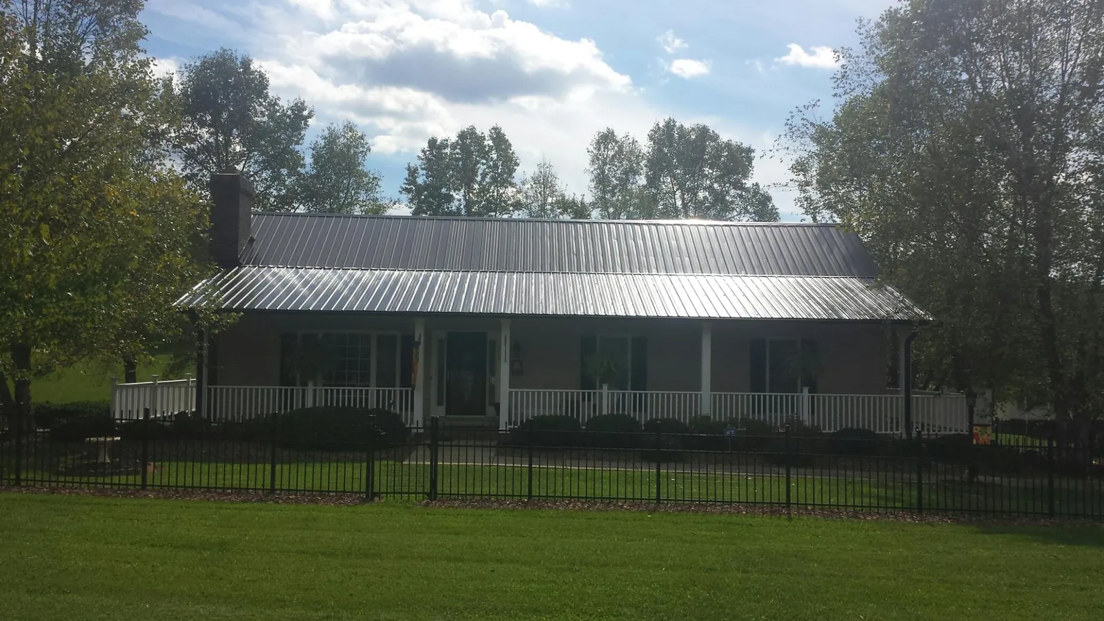 Gray metal roof on a brick ranch with a full width front porch — Gutter Guard Installation work by our crew in Carlos
