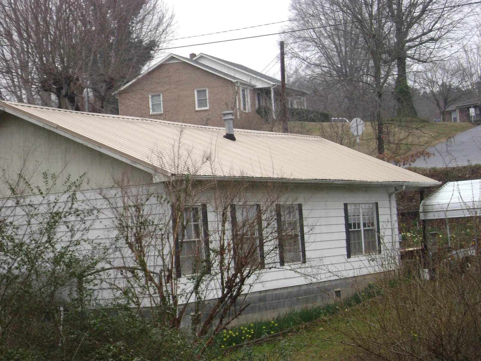 Tan metal roof on a white sided house set into a hillside — Commercial Roofing by Roofing Brothers in Carlos