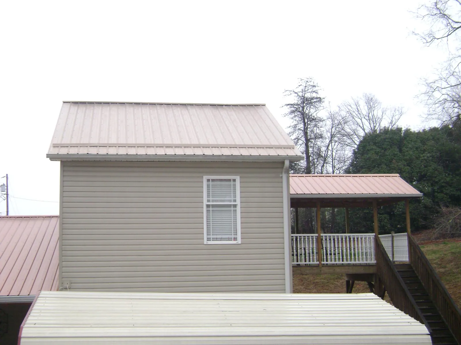Tan metal roofs on a two story addition and attached porch, from a Roof Replacement job in Carlos